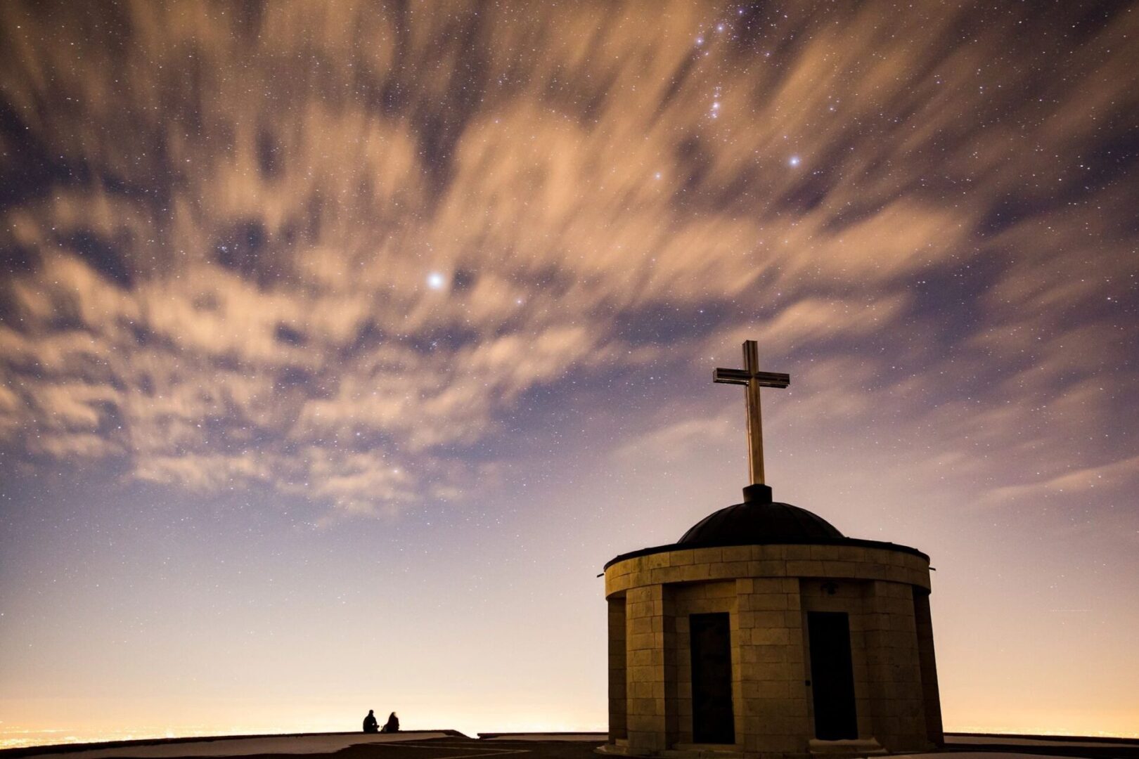 A silhouetted chapel with a cross under a cloudy, twilight sky. A silhouetted chapel with a cross under a cloudy, twilight sky.