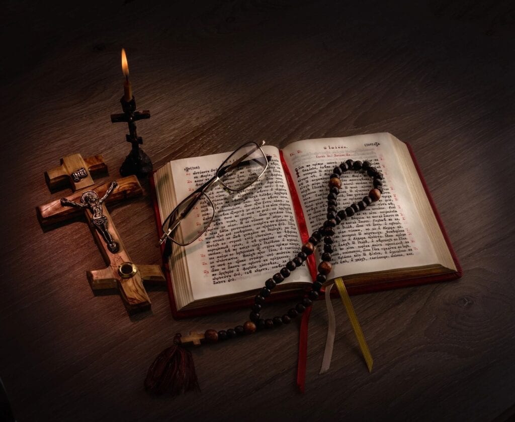 An open Bible with rosary beads and a wooden cross in dim light.