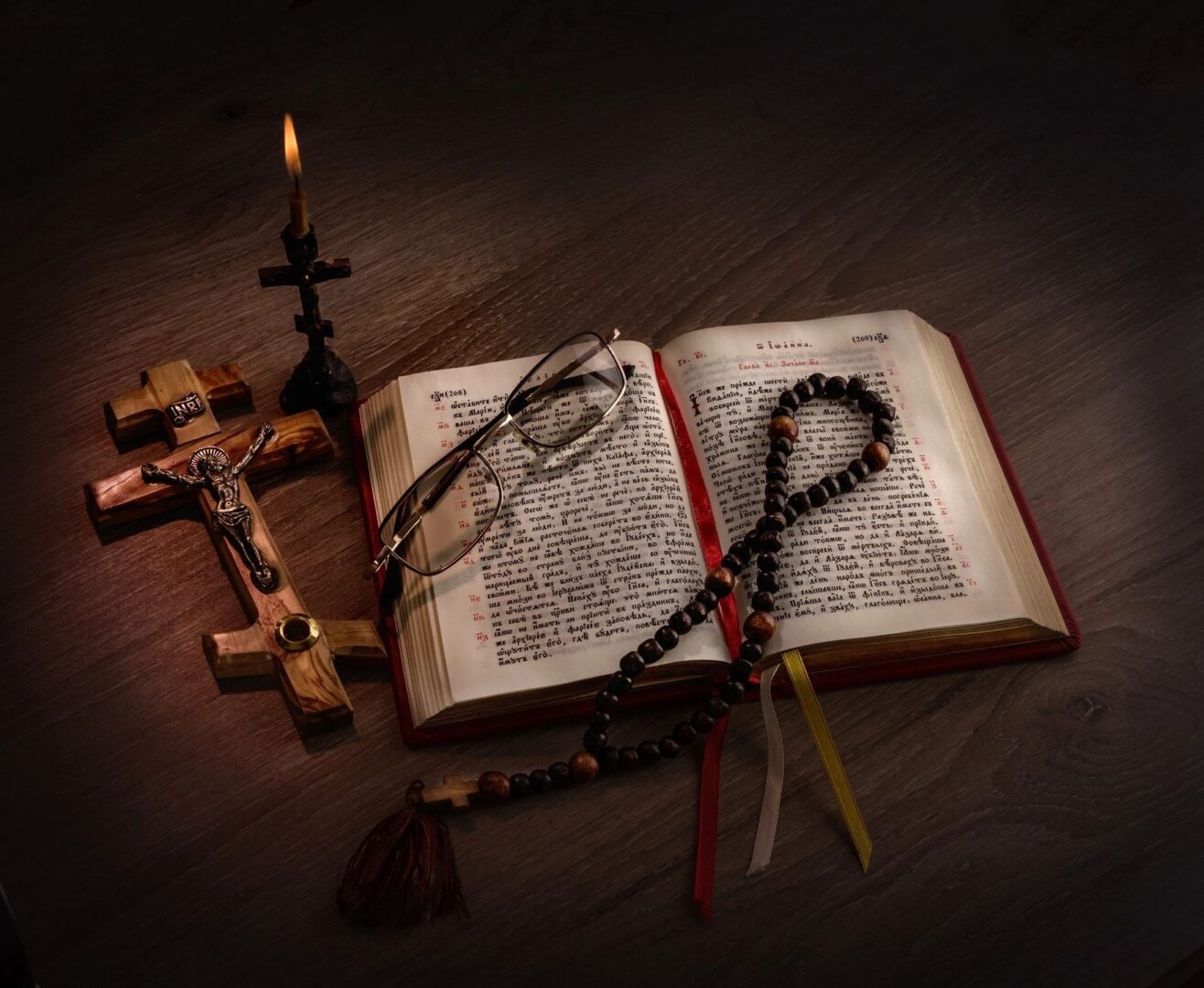 An open Bible with rosary beads and a wooden cross in dim light. An open Bible with rosary beads and a wooden cross in dim light.
