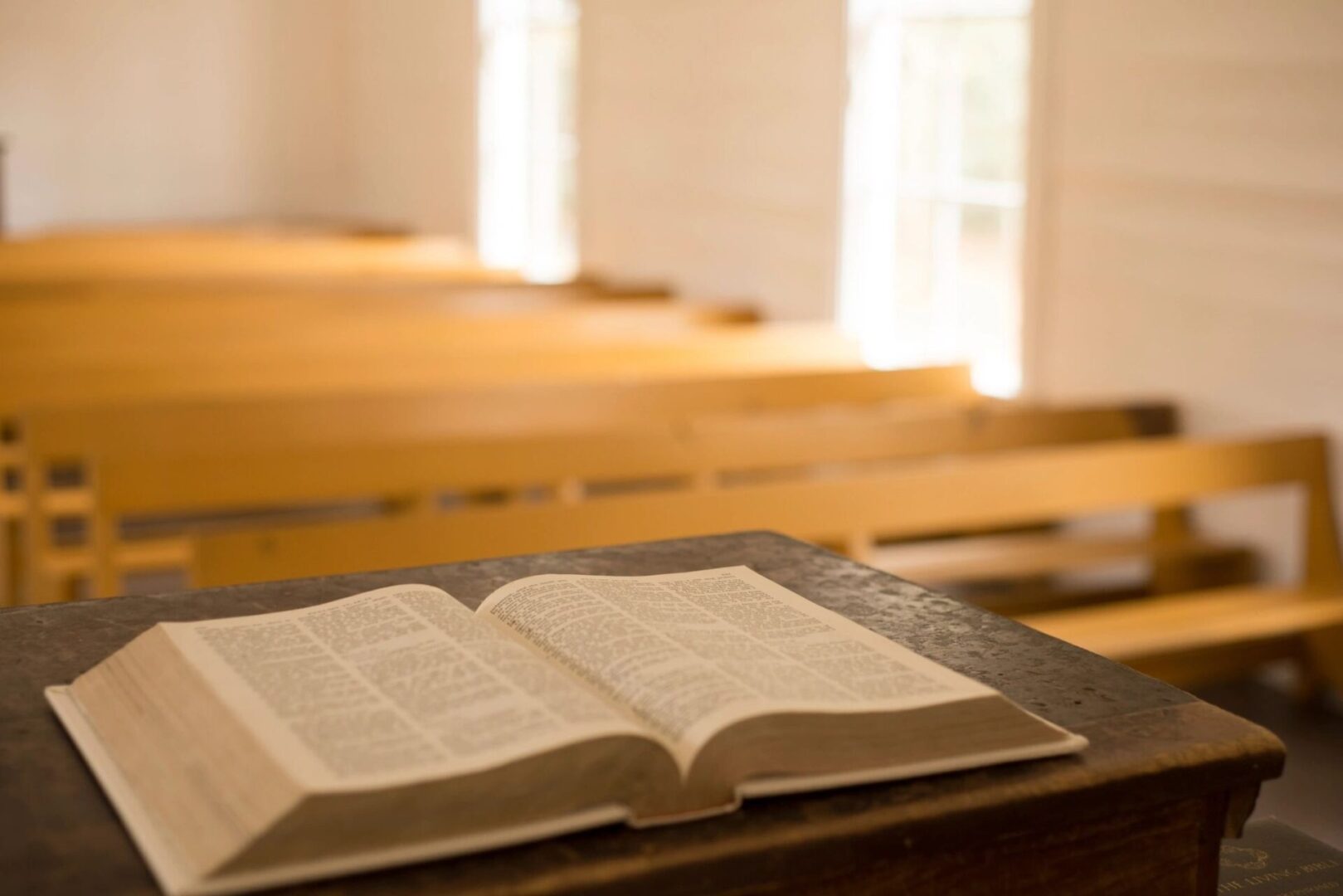 An open Bible rests on a wooden surface in a sunlit church. An open Bible rests on a wooden surface in a sunlit church.