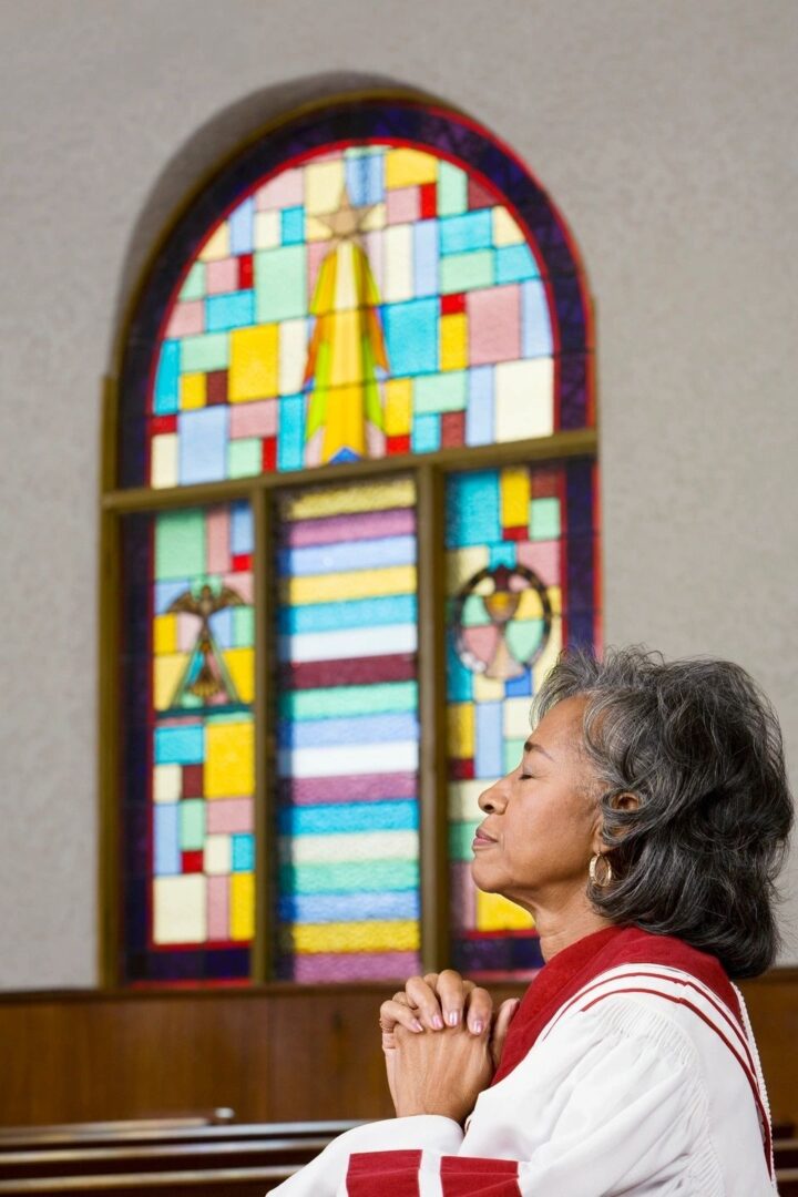Elderly woman gazing thoughtfully at a colorful stained glass window. Elderly woman gazing thoughtfully at a colorful stained glass window.