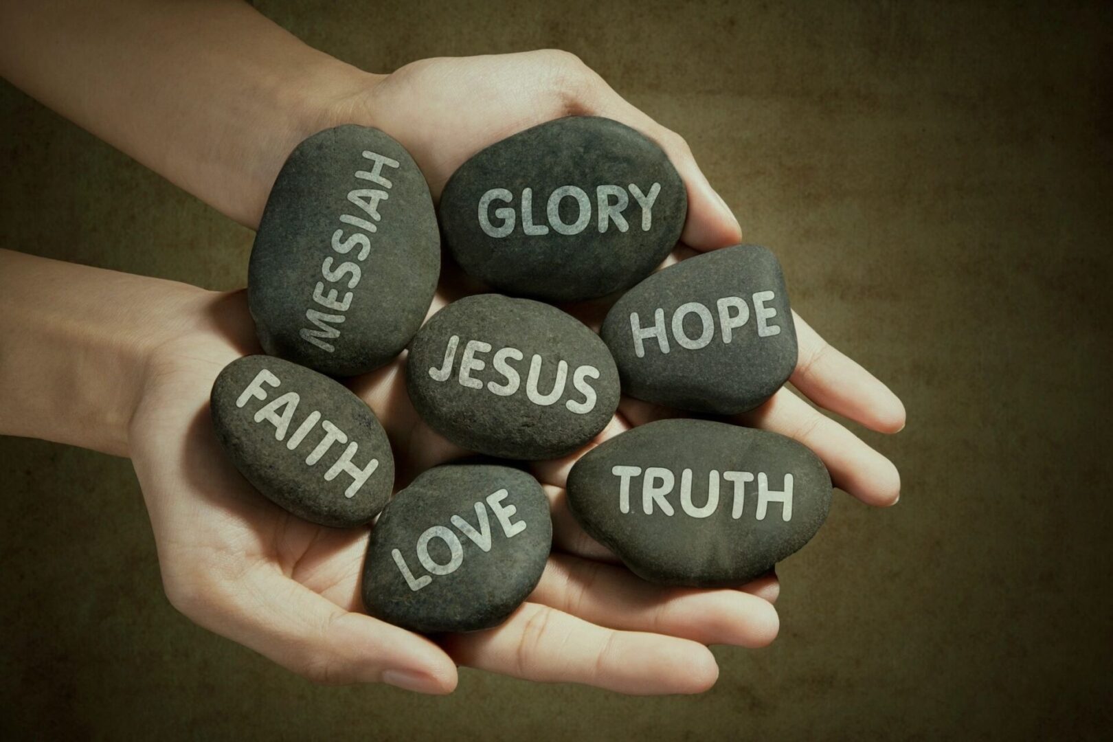 Hands holding up smooth rocks with the words “Jesus,” “faith,” “Messiah,” and other related terms