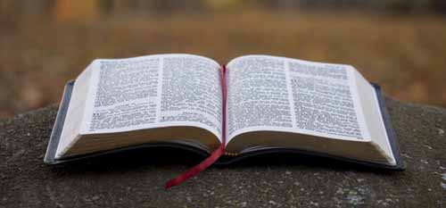 An open book with a red ribbon bookmark lying on a textured surface. An open book with a red ribbon bookmark lying on a textured surface.