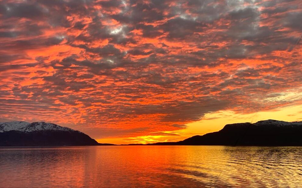 Vibrant orange and red sunset over calm water between silhouetted hills. Vibrant orange and red sunset over calm water between silhouetted hills.
