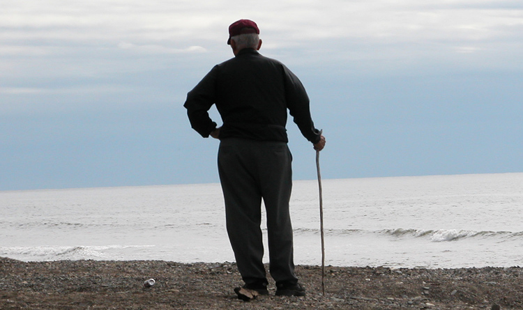 Man standing by the water with a walking stick, gazing at the horizon. Man standing by the water with a walking stick, gazing at the horizon.