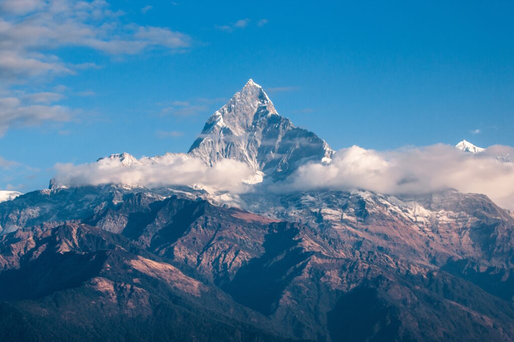 Snow-capped mountain peak rising above clouds under a clear blue sky.